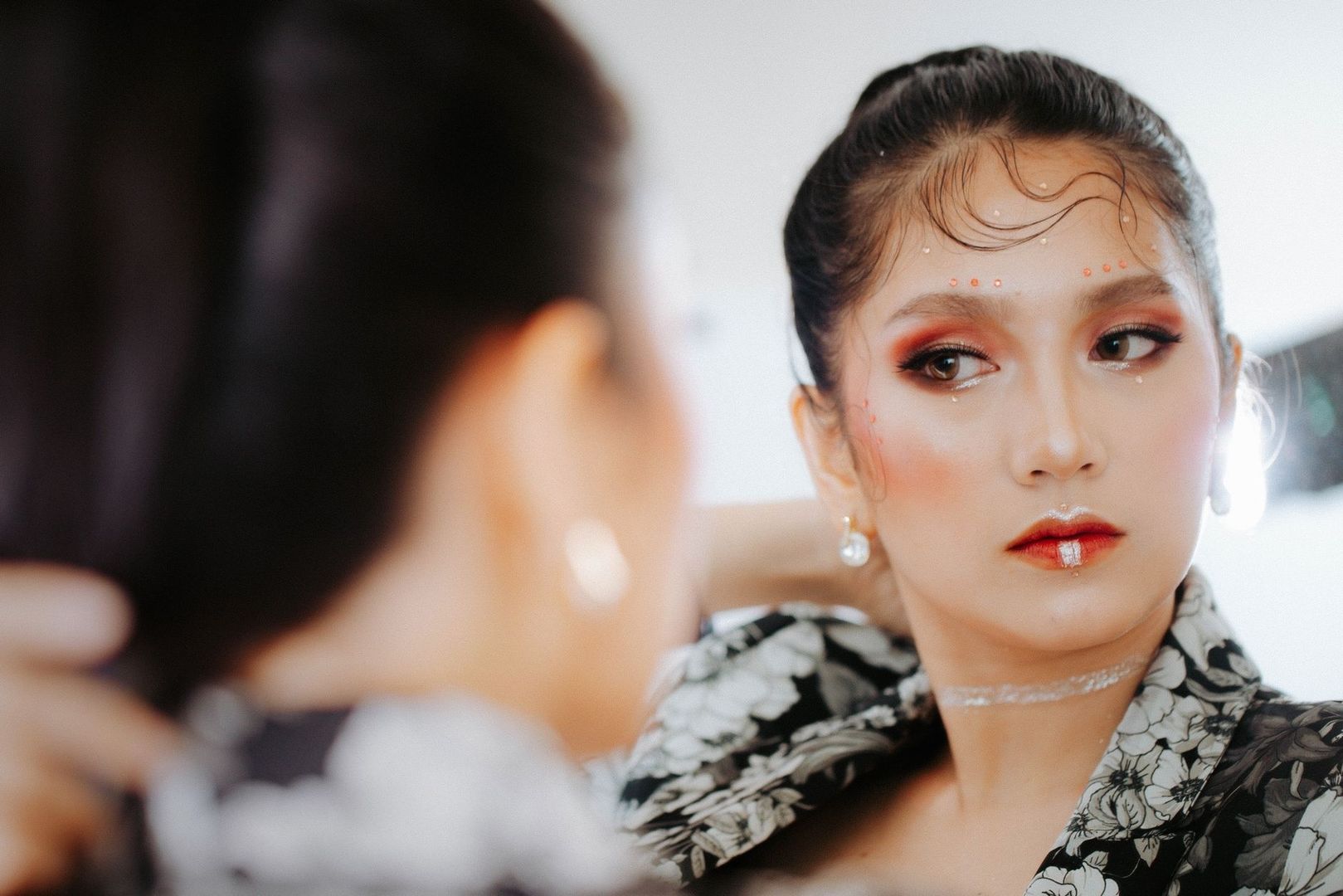Närbild av kvinna med glansig bas och grafisk ögonmakeup framför en spegel